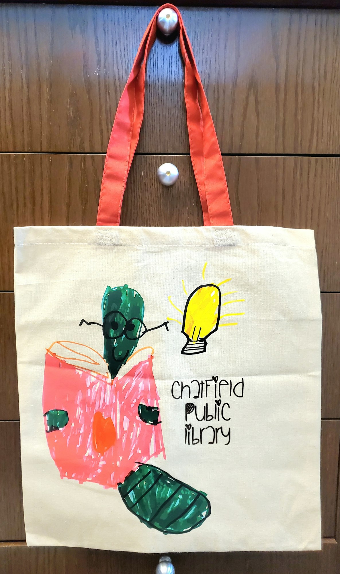 Tote bag with a colorful drawing of a creature, book, and lightbulb. Text: "Chatfield Public Library."