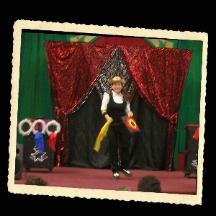 A person performing on stage with a juggling club, wearing a hat, near a curtain backdrop, with hoops on the side.