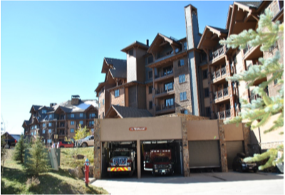 A fire station with two trucks in a mountain resort area, flanked by multi-story buildings with balconies.