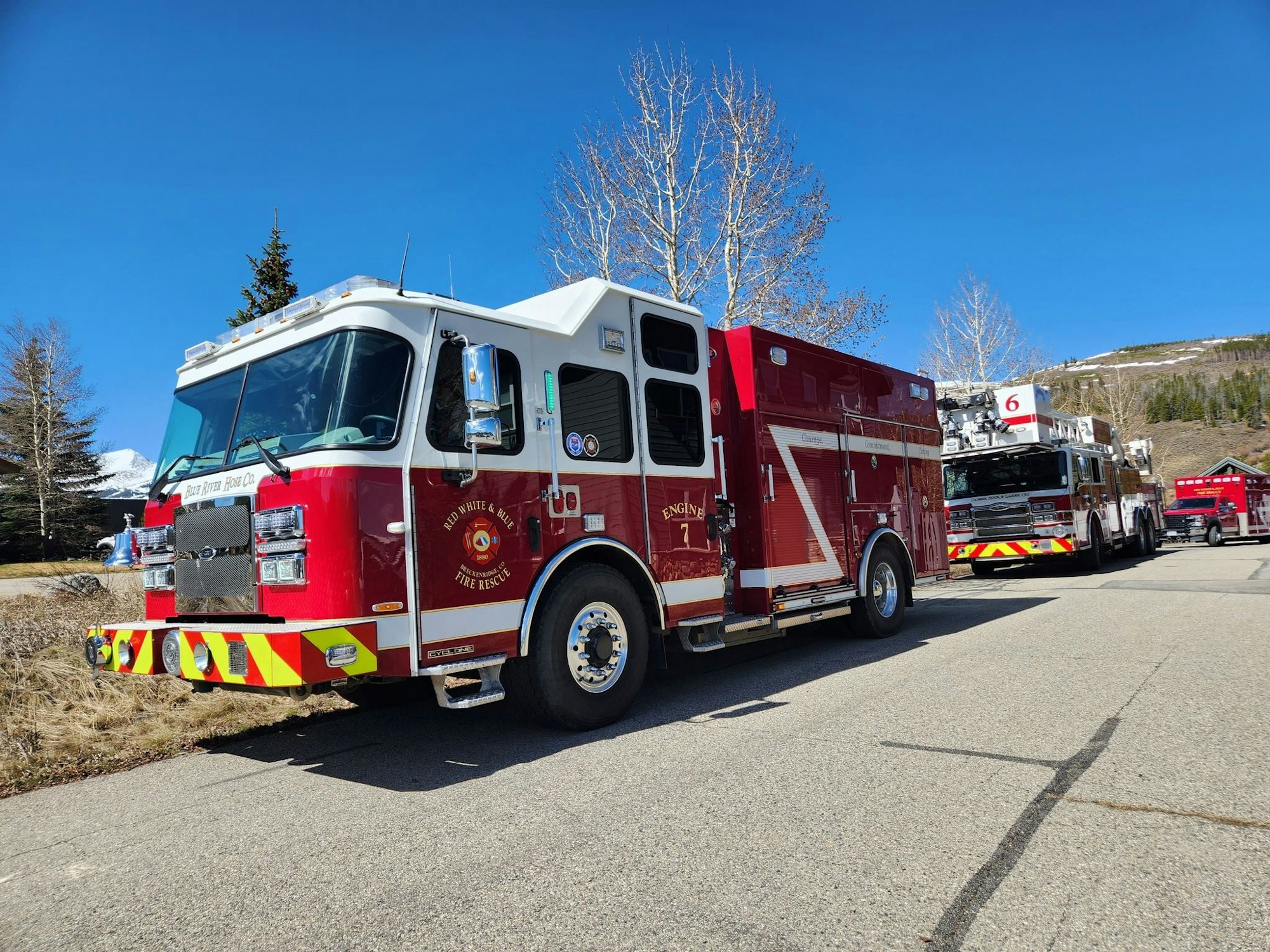 A row of fire trucks parked on a sunny day with clear skies and trees nearby.