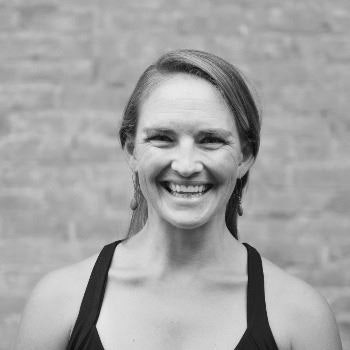 A smiling woman in a black tank top, black and white photo, brick wall background.