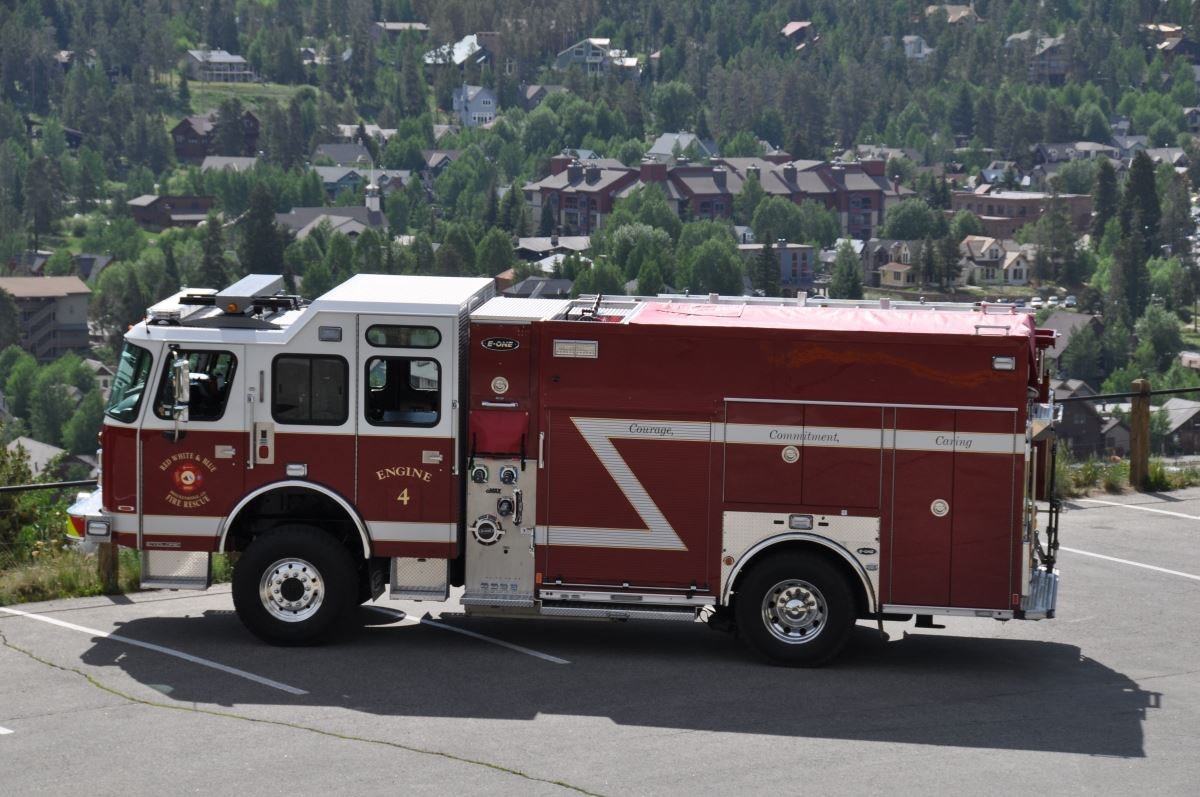 A fire engine parked on a road with houses and trees in the background.