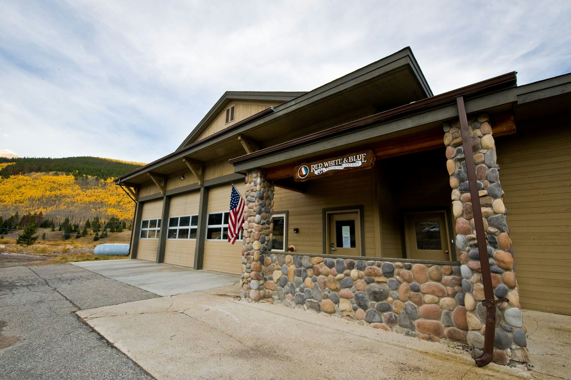 A building with a sign "Red White & Blue," an American flag, surrounded by autumn colored trees.