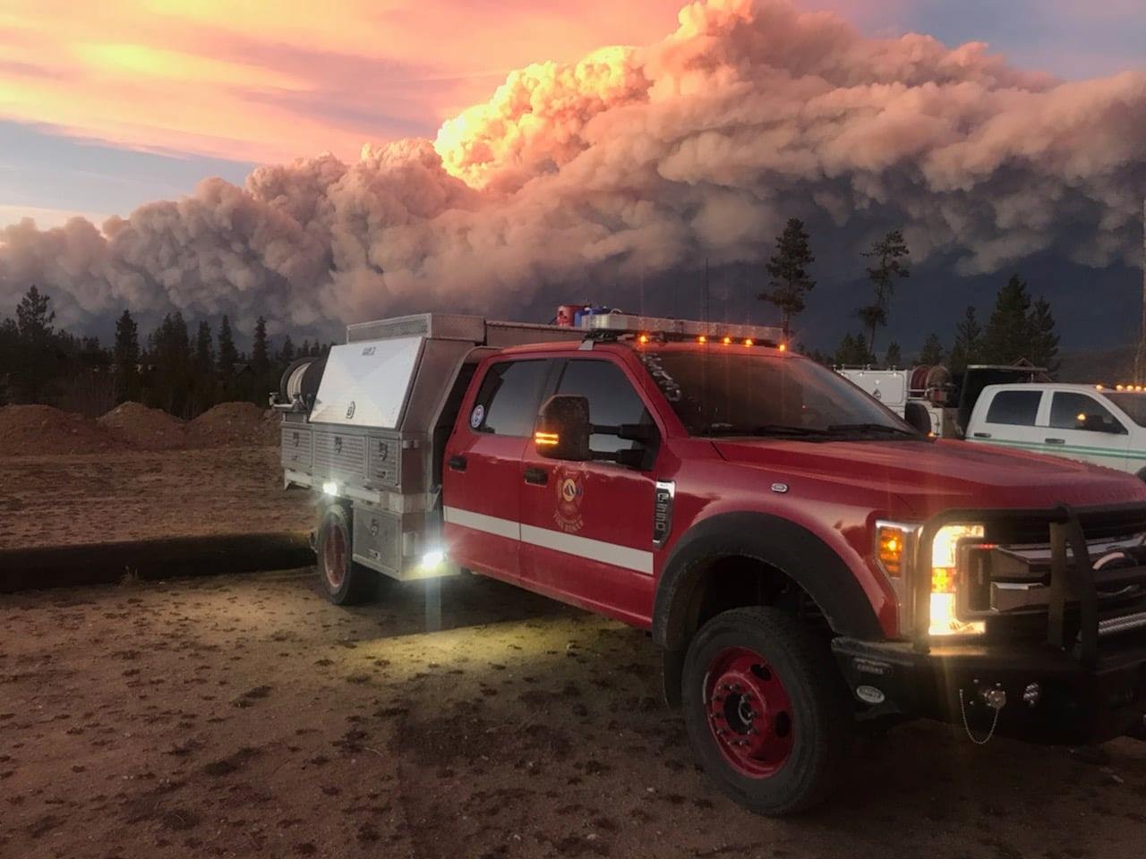 A fire truck with a massive smoke cloud in the background at twilight.