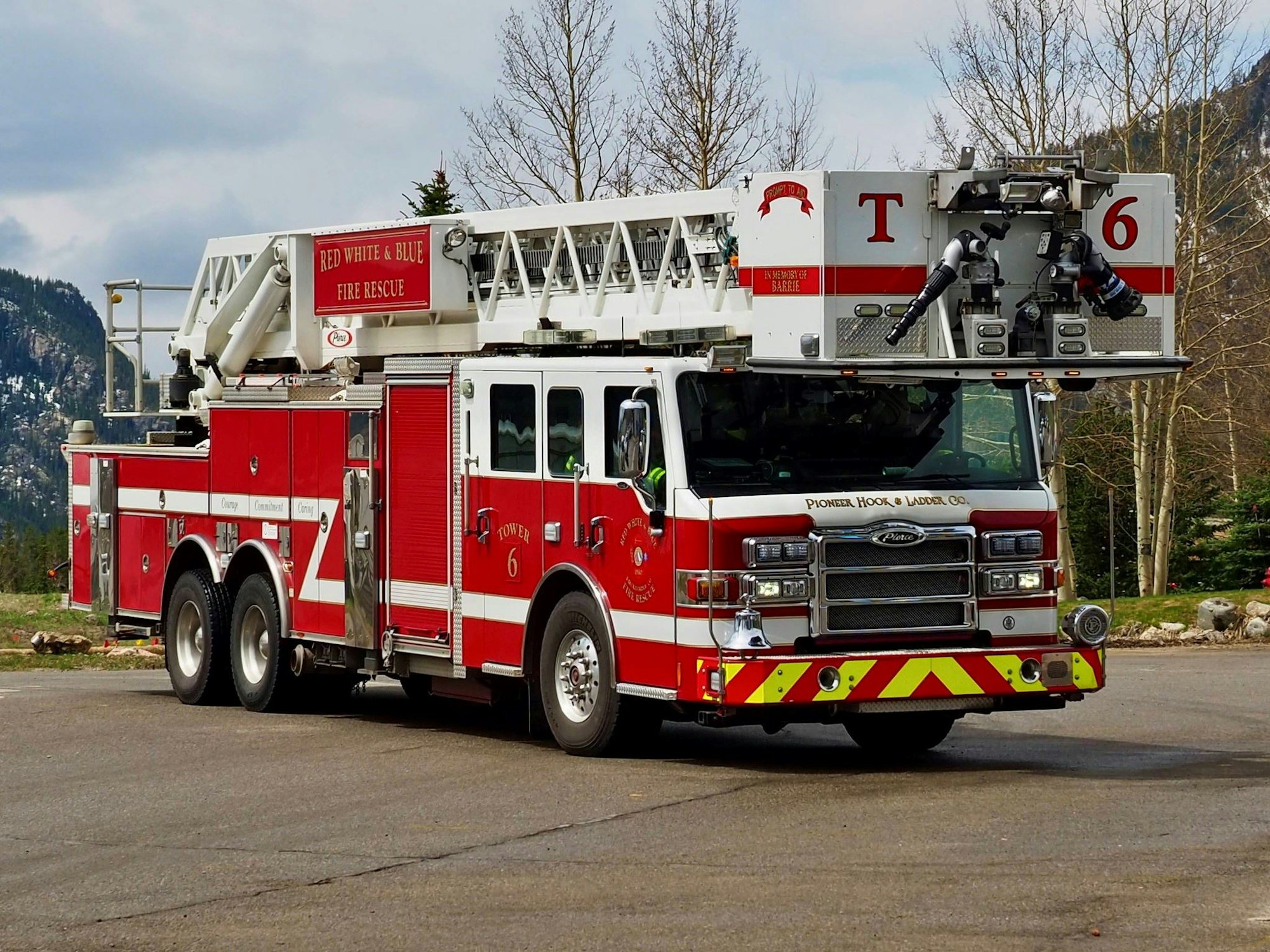 A red firetruck with a ladder parked outdoors with mountains in the background.