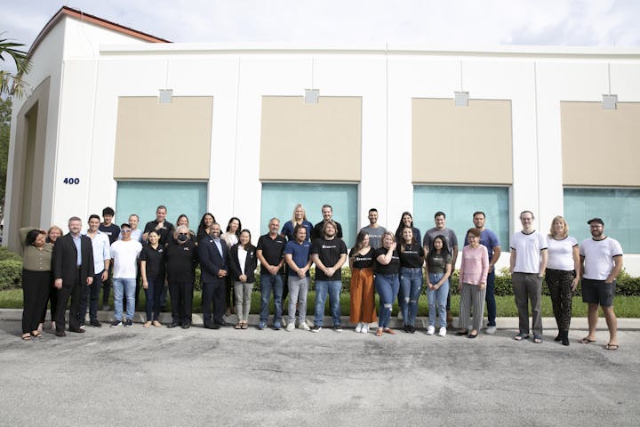 A diverse group of people poses for a photo outside a building, smiling and dressed in casual attire.