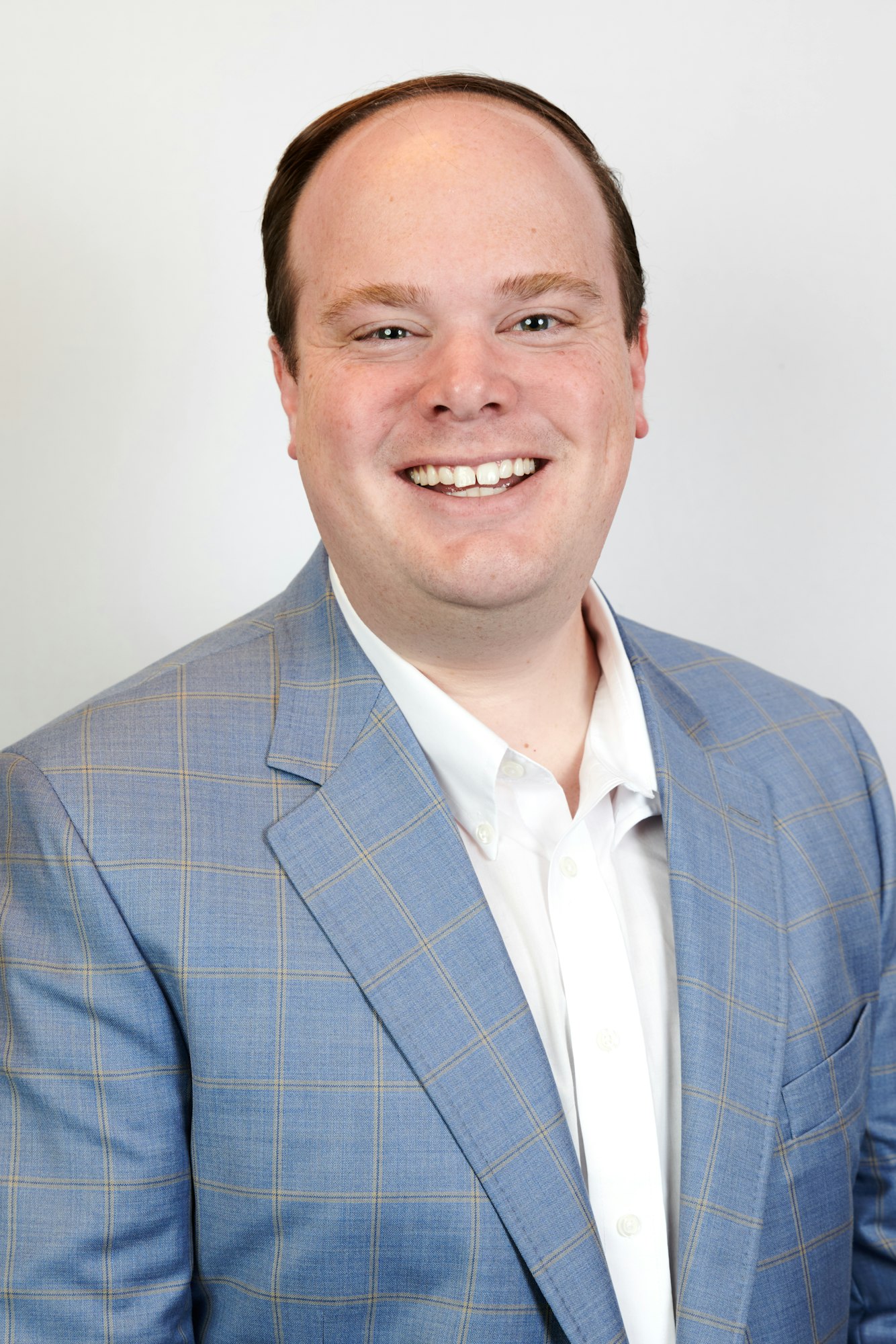 A smiling person in a plaid blazer over a white shirt against a light background.