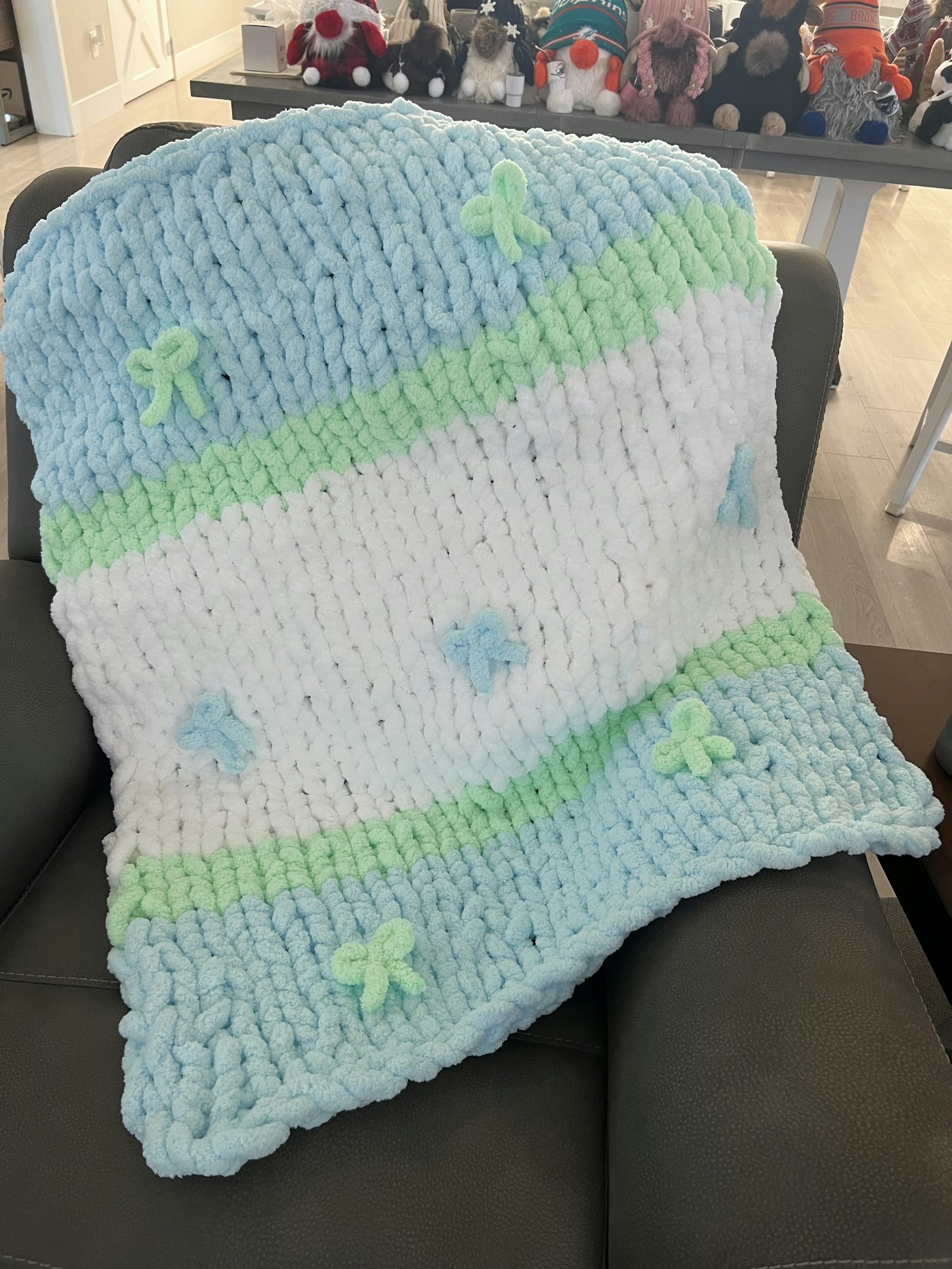 A fluffy, knitted blanket with white, green, and blue stripes and small decorative bows.