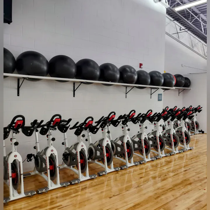 A fitness studio with several indoor cycling bikes aligned in rows and stability balls on a shelf above.