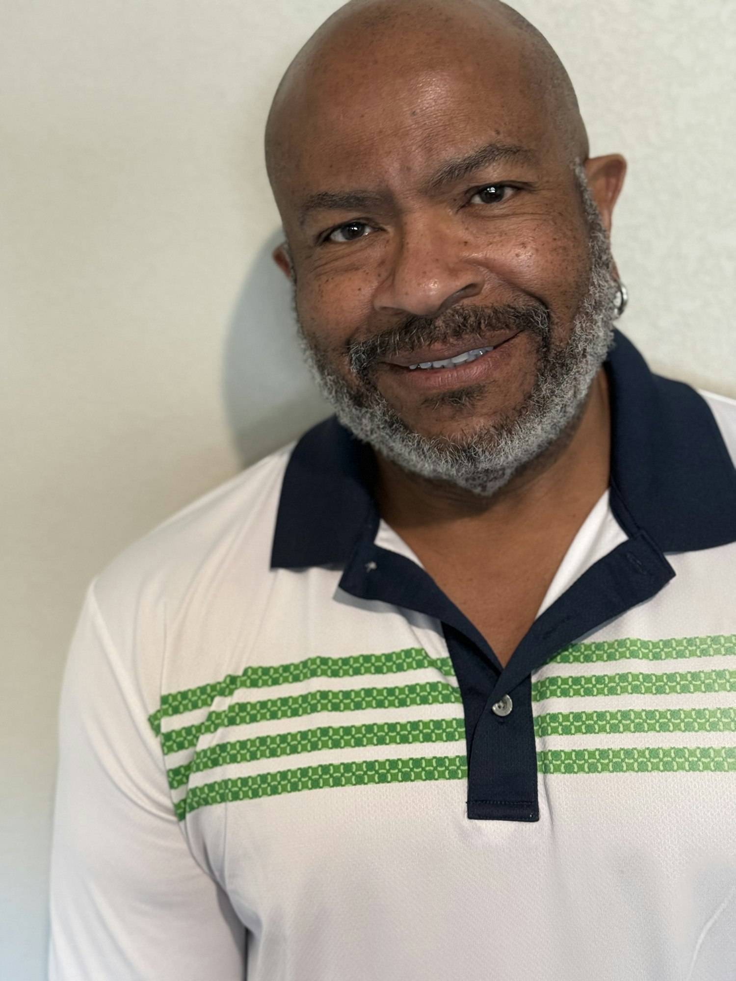 A person with a beard, wearing a white shirt with green stripes and a dark collar, smiling at the camera.
