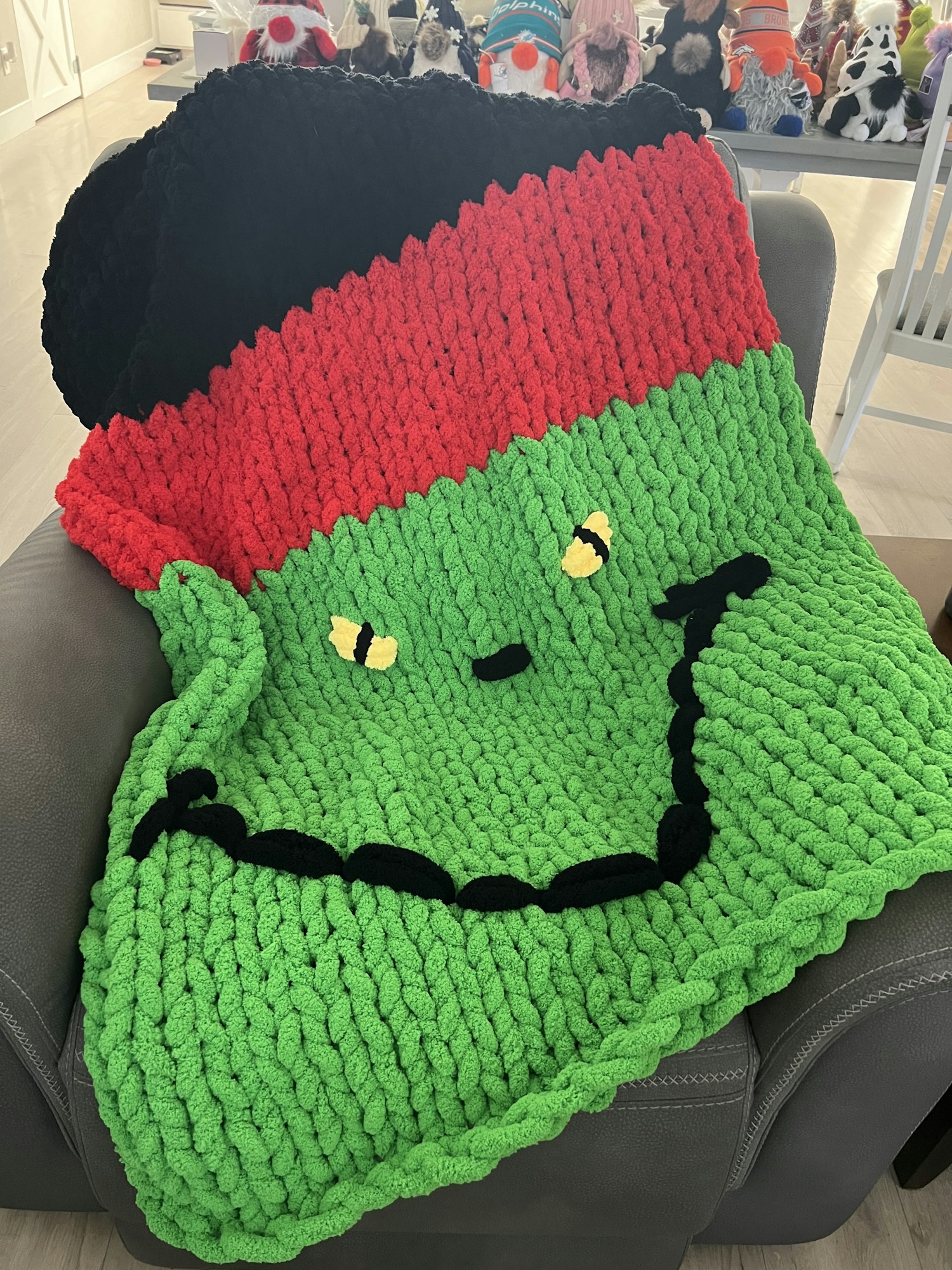 A knitted blanket featuring a cartoonish green face with red and black hair, likely resembling a classic monster.