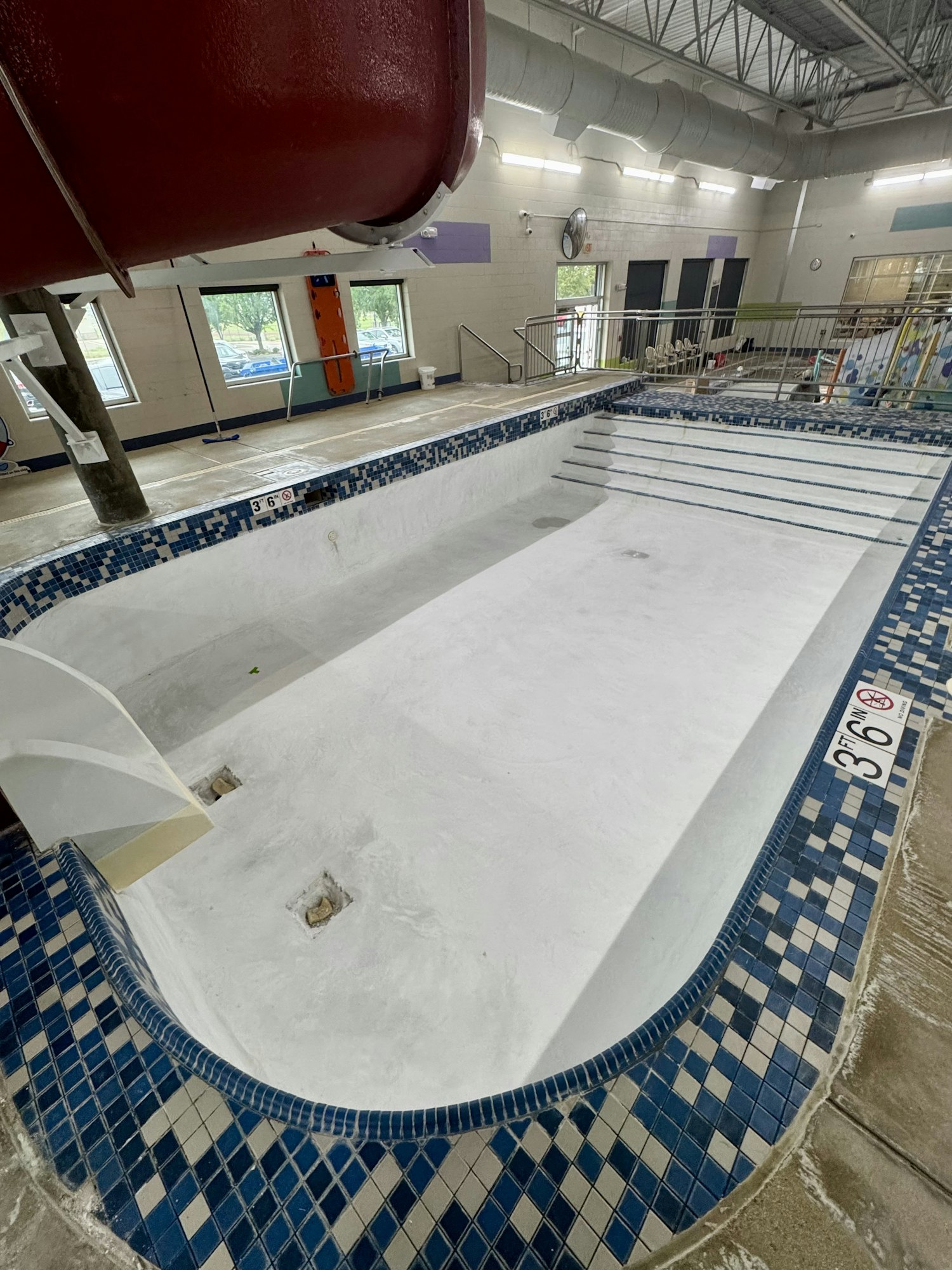 An empty indoor swimming pool with a waterslide and tiled edges, located in a recreational facility.