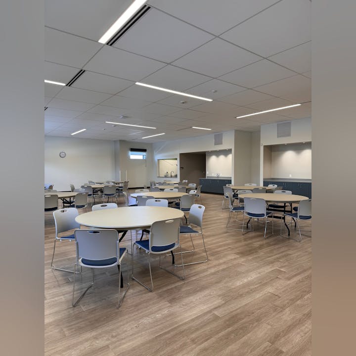 A room with round tables and chairs on a wooden floor, ceiling with lights and a clock.