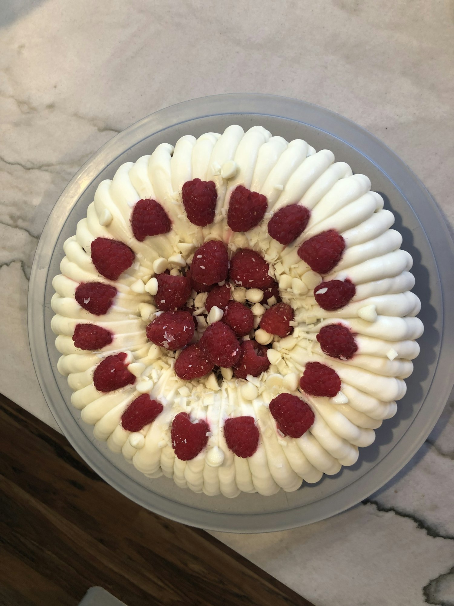 A round cake topped with white frosting, raspberries, and white chocolate chips.