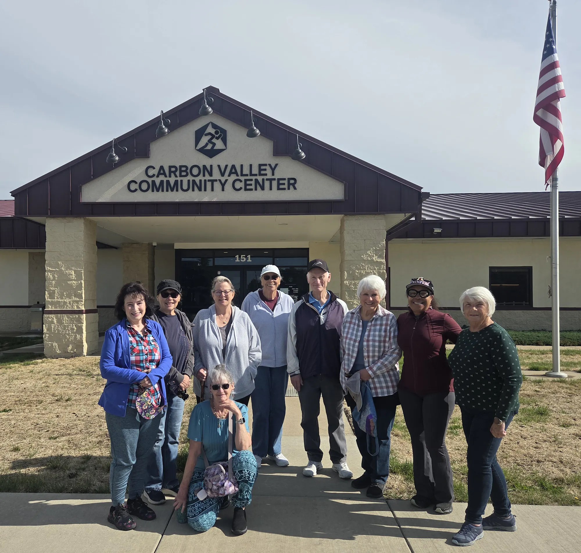 A group of people stands outside the Carbon Valley Community Center, smiling and posing for a photo.