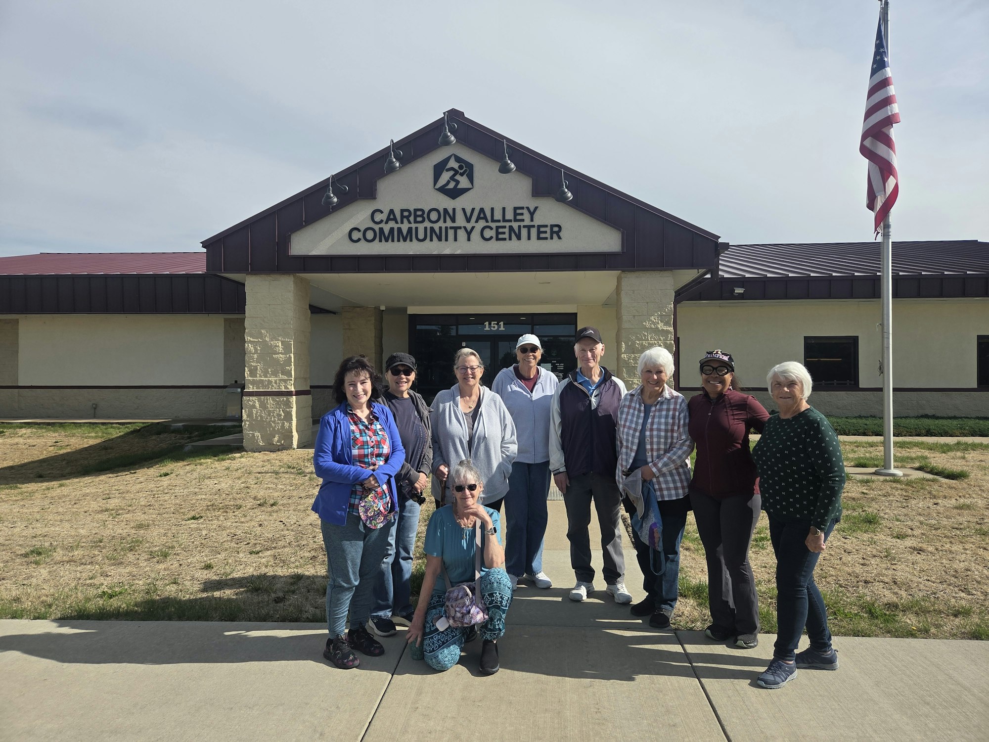 A group of people stands outside the Carbon Valley Community Center, smiling and posing for a photo.