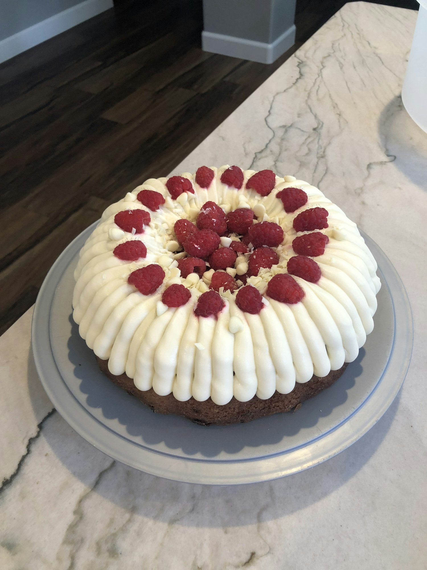 A cream-frosted cake topped with raspberries on a grey plate.