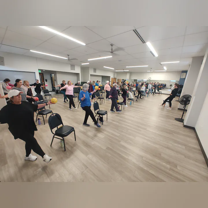 A group exercise class with participants holding weights while seated in chairs, engaging in fitness activities together.