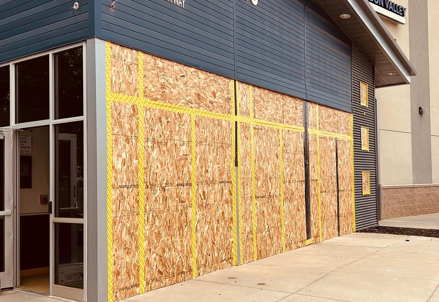 A storefront with windows boarded up using wooden panels and yellow tape.
