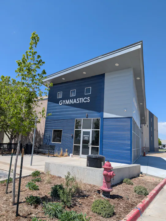 A modern gymnastics facility with blue siding, a welcoming entrance, and landscaping featuring a red fire hydrant.