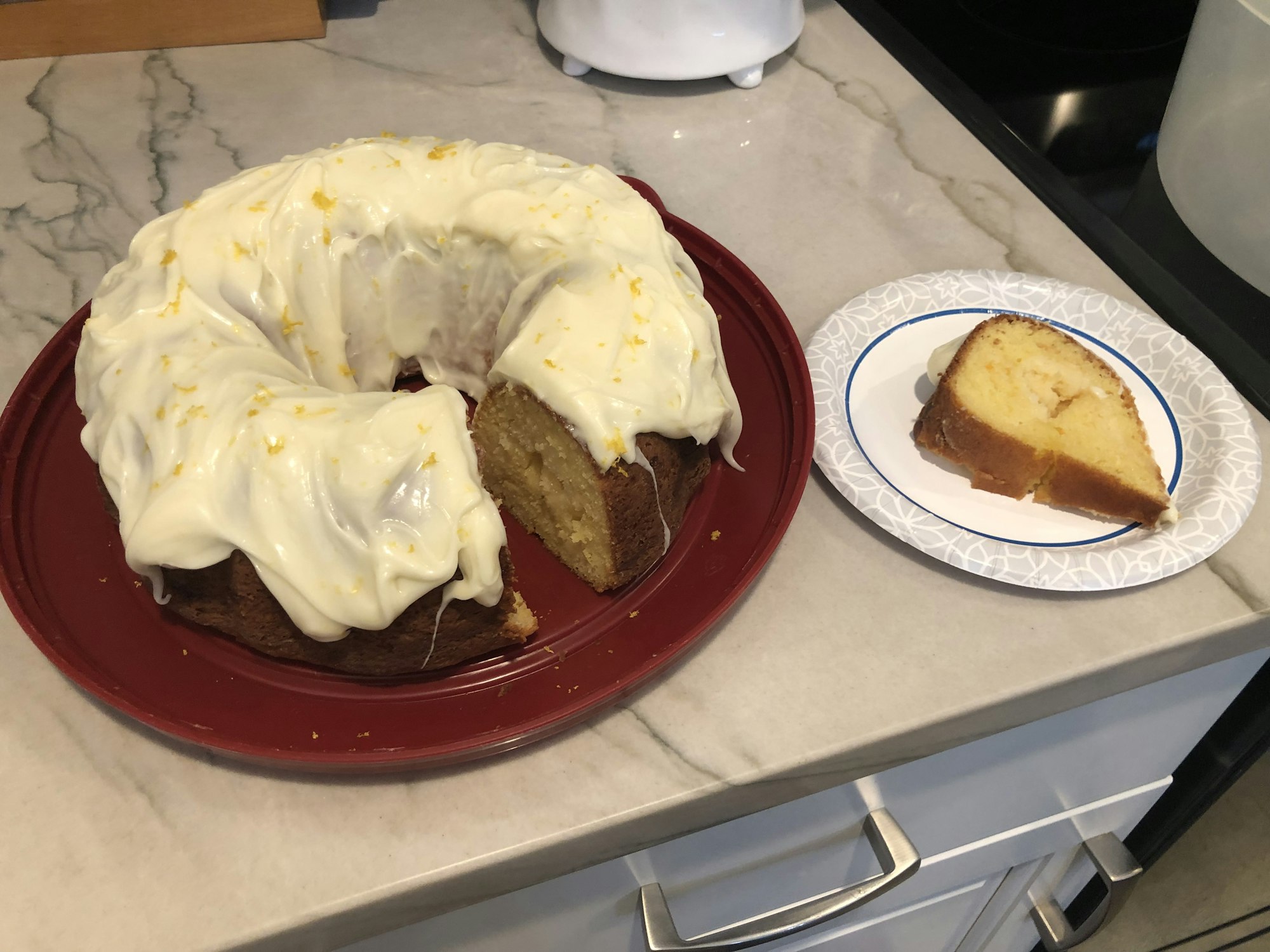 A frosted Bundt cake with a slice cut out, displayed on a countertop.