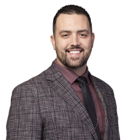 A man in a plaid suit, maroon shirt, and black tie, smiling at the camera.