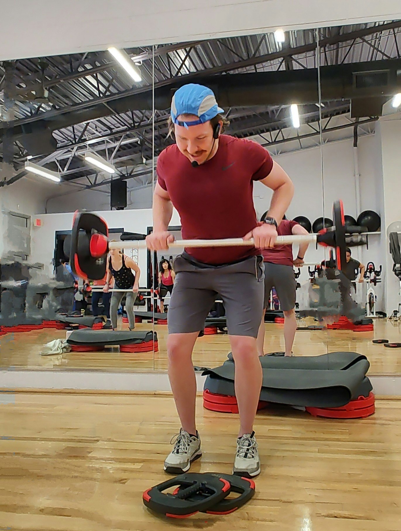 A person exercising in a gym, lifting a barbell, with workout equipment and mirrors in the background.