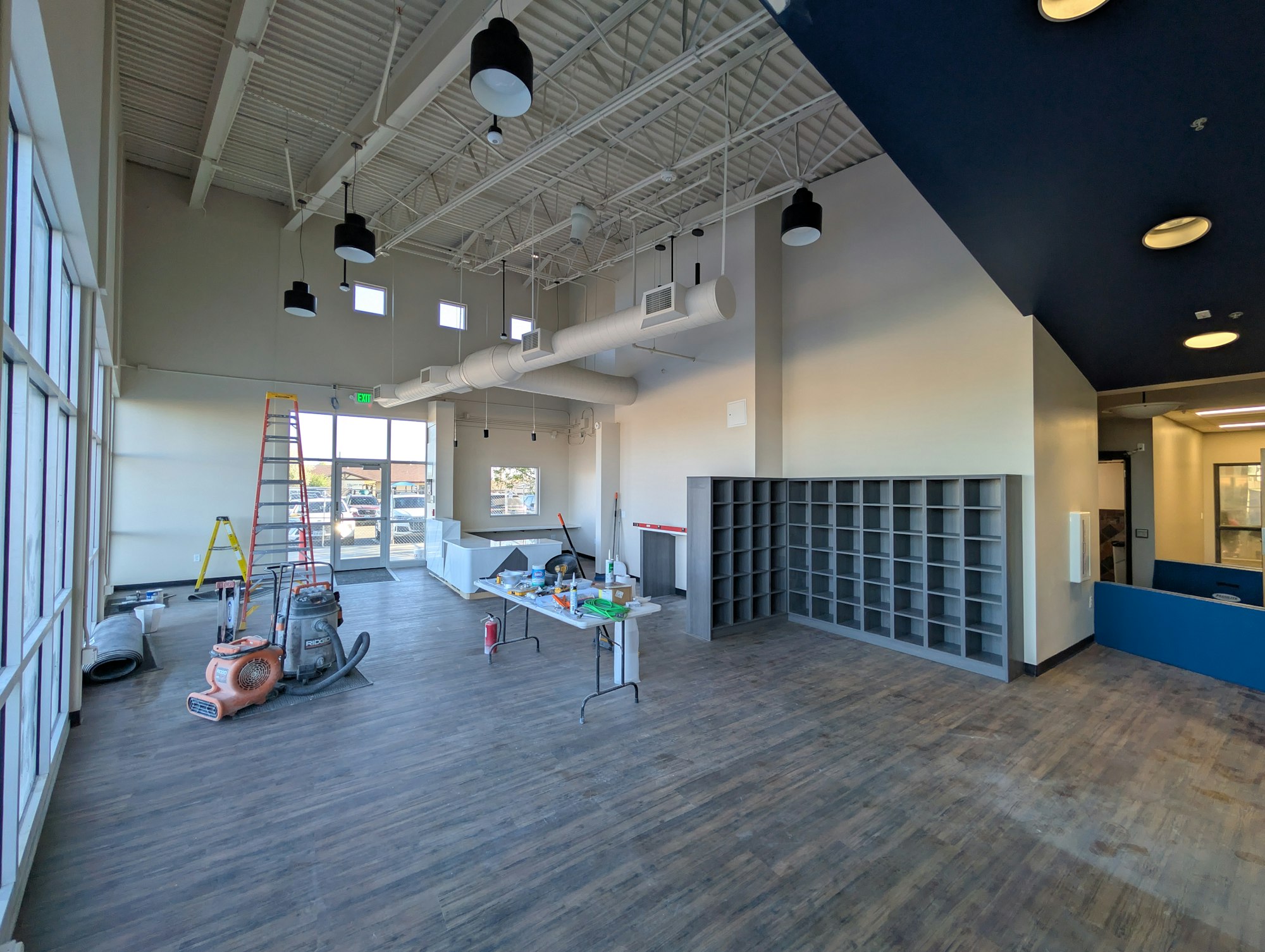 The image shows an unfinished interior space with a ladder, tools, and furniture in a modern layout.