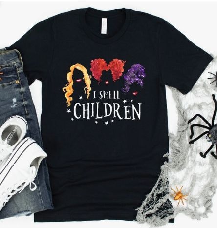 Black t-shirt with colorful wigs and text "I Smell Children," surrounded by jeans, sneakers, and Halloween decor.