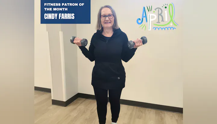 A smiling woman holds dumbbells, recognized as April's Fitness Patron of the Month, Cindy Farris.