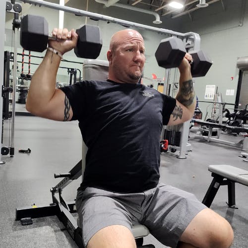 A person is doing seated shoulder presses with dumbbells in a gym.
