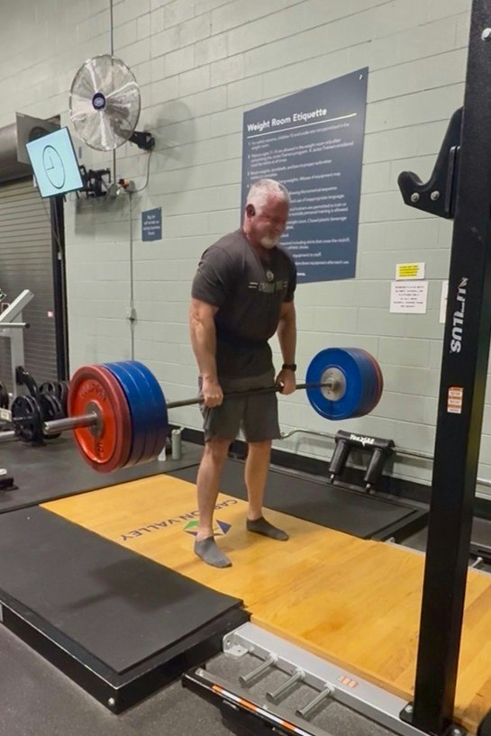 A muscular person is lifting a heavy barbell with weights in a gym setting, focusing on deadlifting technique.