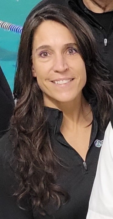 A person with long dark hair wearing a black top, smiling.