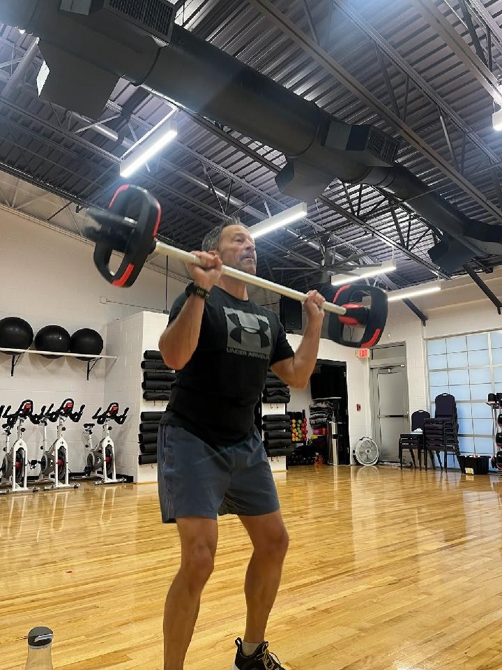 Person lifting a barbell in a gym, with exercise equipment and mirrors in the background.