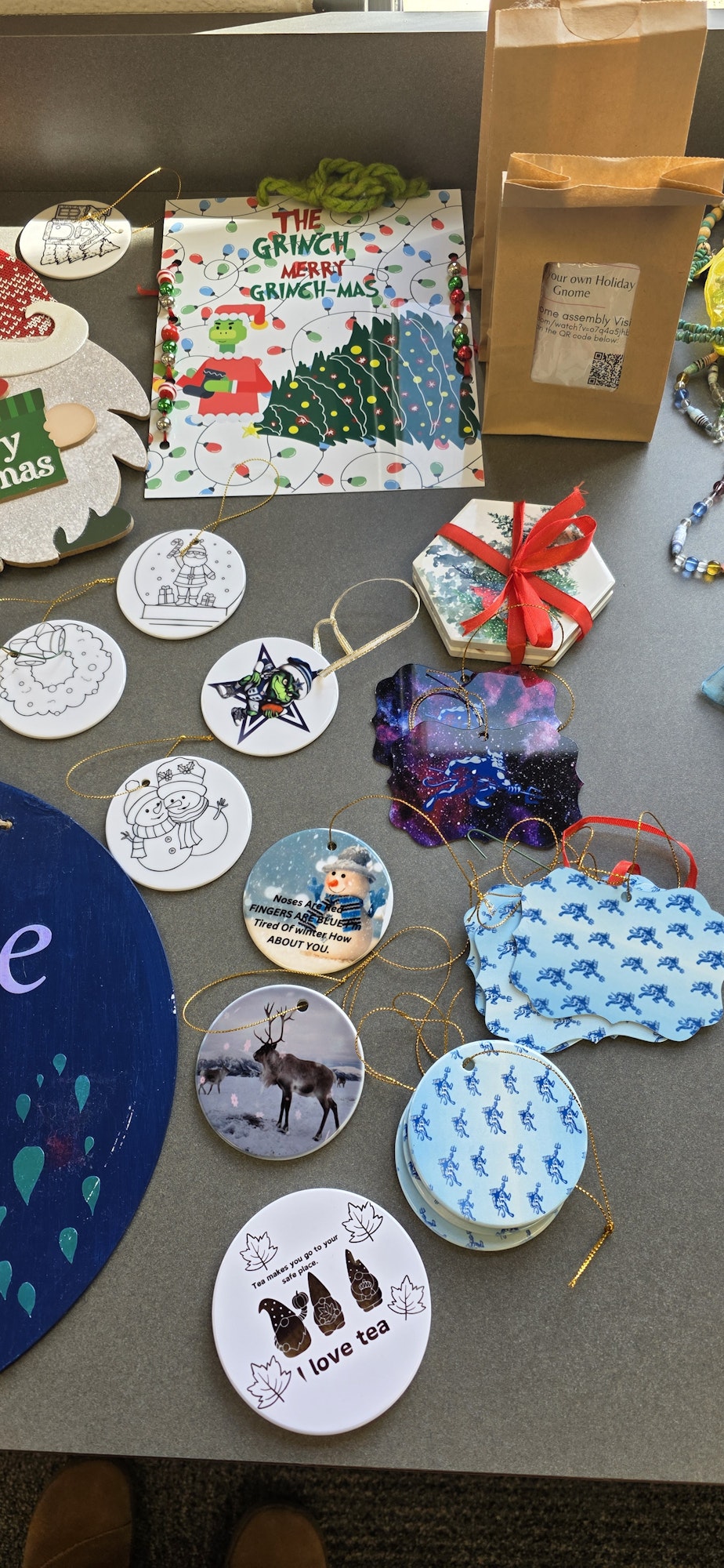 A collection of holiday-themed ornaments and decorations, including a Grinch book, coasters, and gift tags on a table.