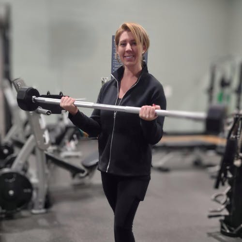 A person in a gym holding a weighted barbell and smiling.