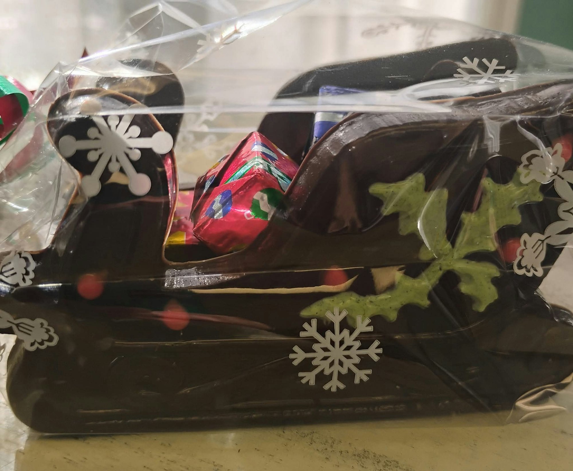 Chocolate sleigh with holly and presents, wrapped in clear plastic with snowflake designs.