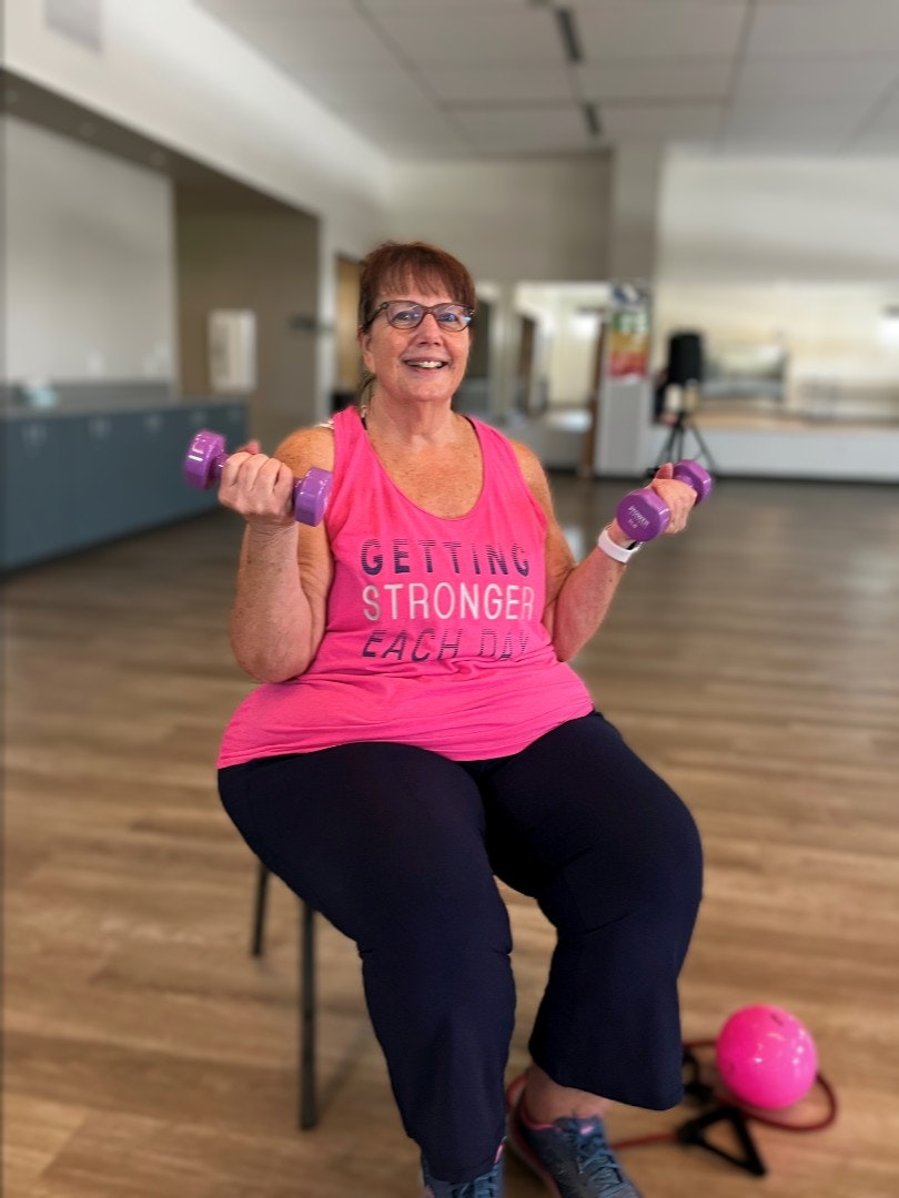 A woman smiling and lifting weights, wearing a shirt with "Getting Stronger Each Day".