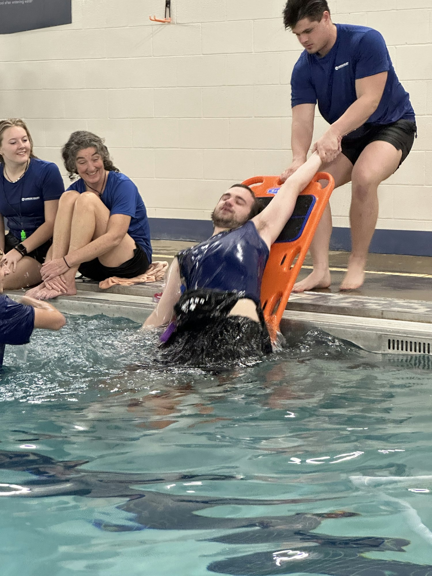 Three people practicing a water rescue drill with a backboard.