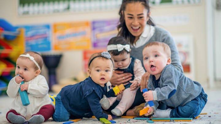 A caregiver and four babies playing with colorful blocks on the floor.