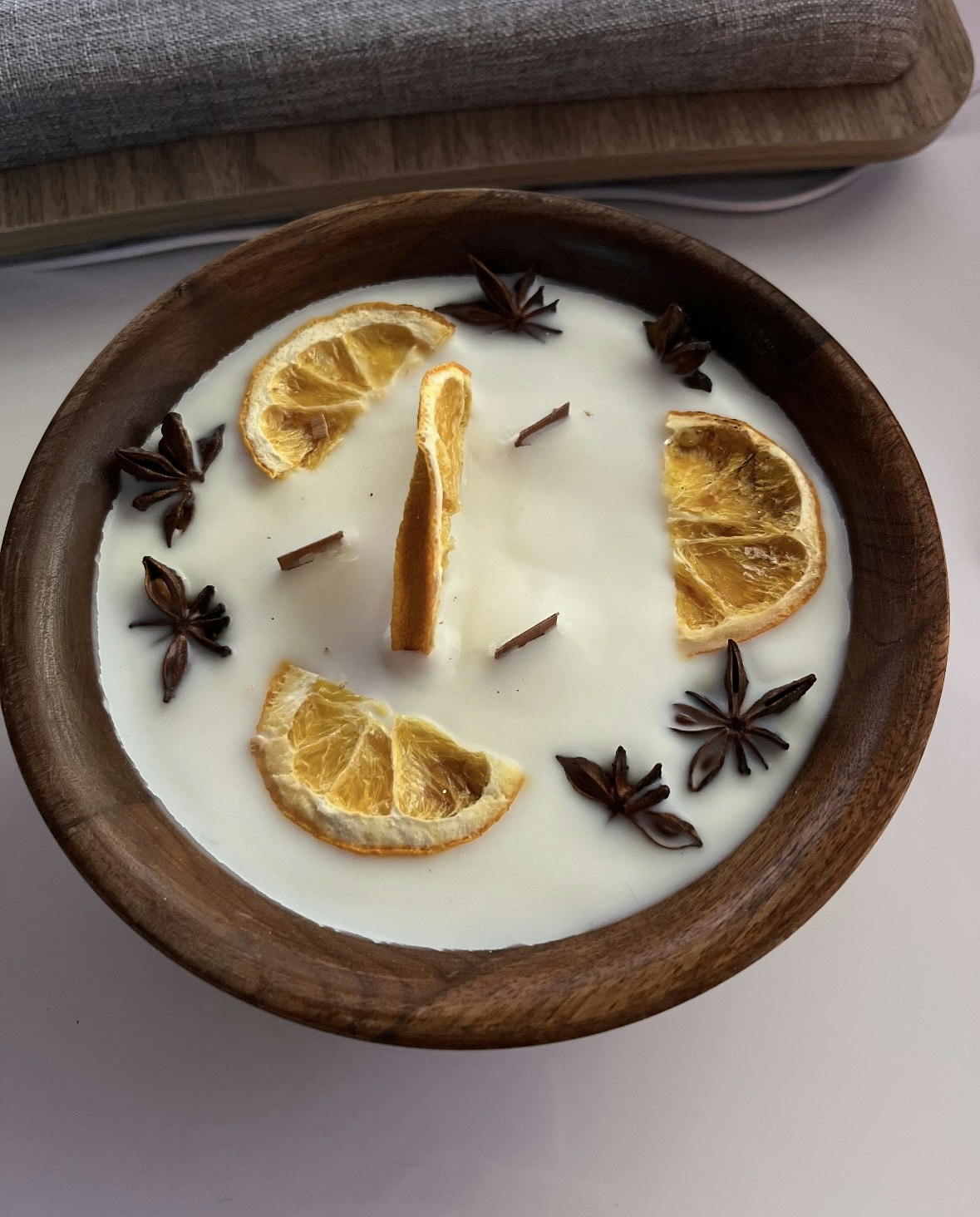 A wooden bowl with white wax, topped with dried orange slices, star anise, and cinnamon sticks.