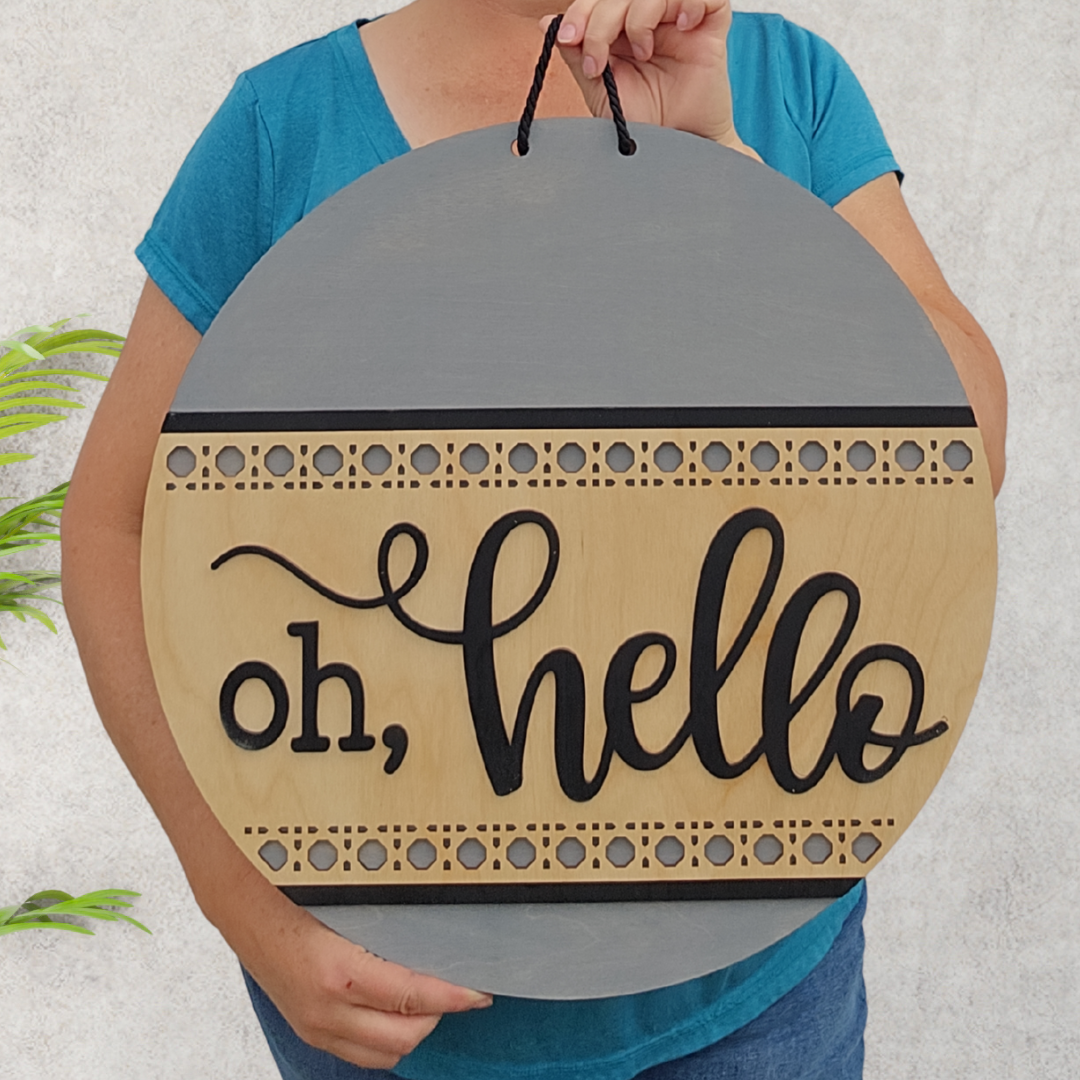 A person holding a round sign with "oh, hello" written on it, decorated with patterns.