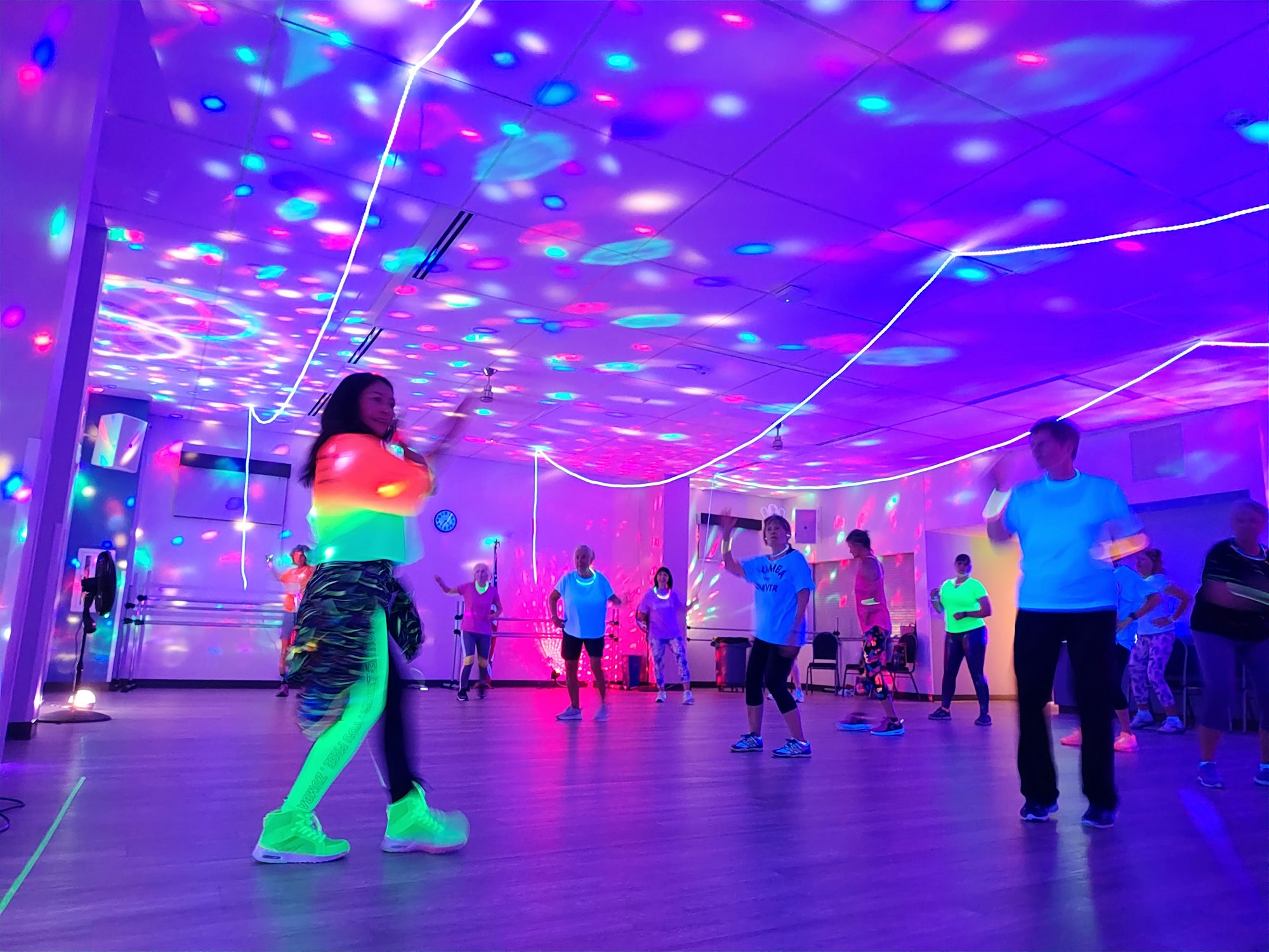 A vibrant fitness class with participants dancing under colorful lights and decorations, creating a lively atmosphere.