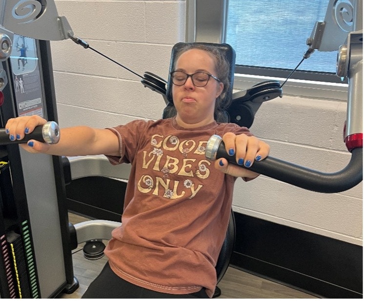 A person on a gym machine with eyes closed, wearing a "Good Vibes Only" shirt, making a funny face.