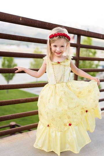 A child smiling in a yellow princess dress and red headband, standing by a railing.