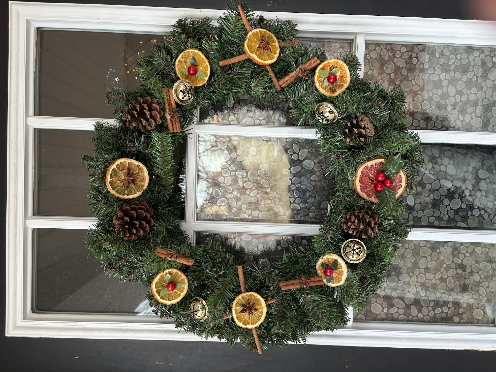 A festive wreath with orange slices, pine cones, cinnamon sticks, and berries on a windowed door.
