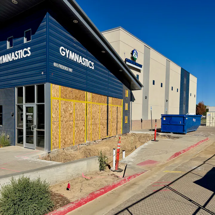 Boarded-up gymnastics building with nearby construction site and a blue dumpster. Signs of renovation or repair work.
