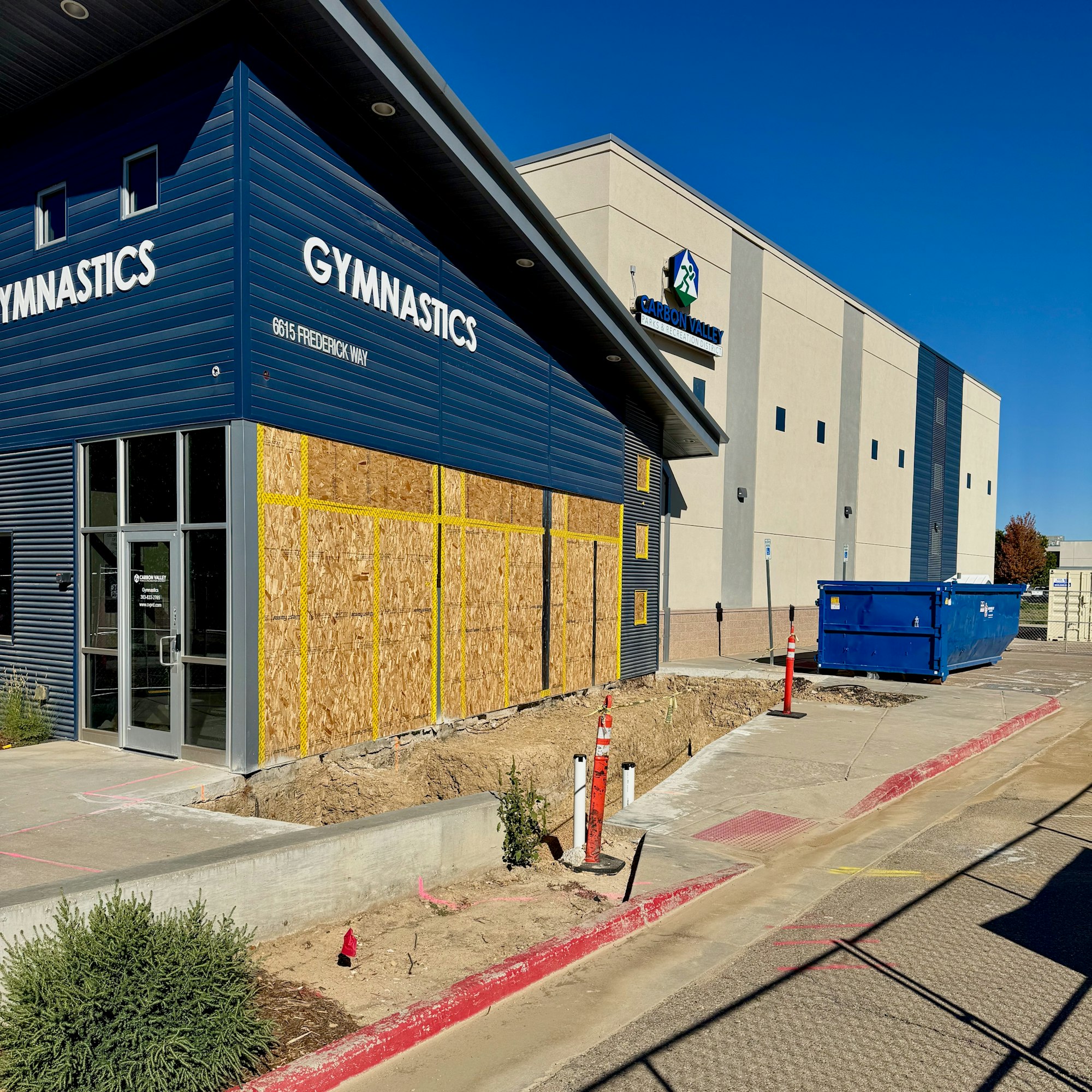 Boarded-up gymnastics building with nearby construction site and a blue dumpster. Signs of renovation or repair work.