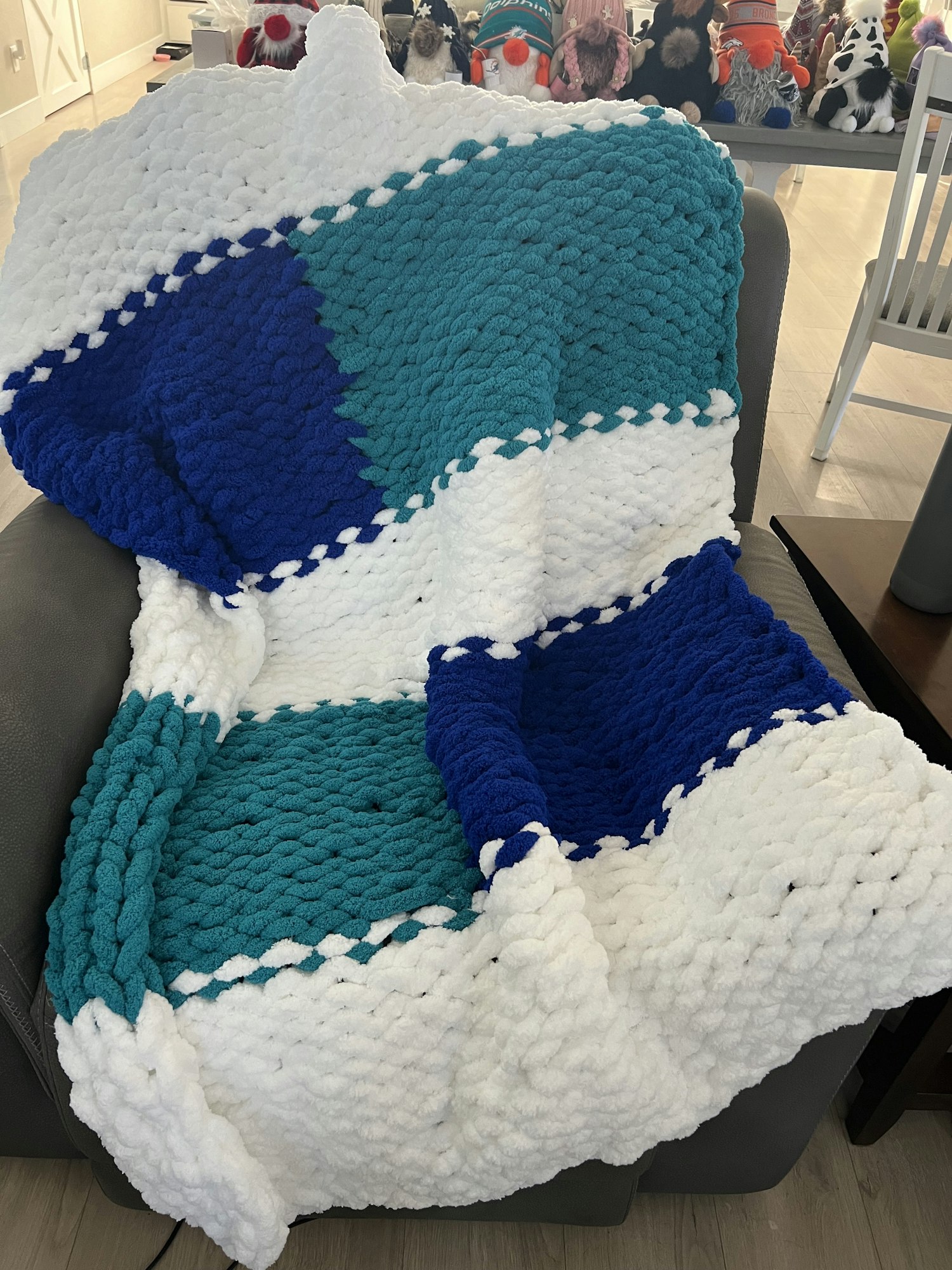 A knitted blanket with white, teal, and blue large stripes, draped over a chair.