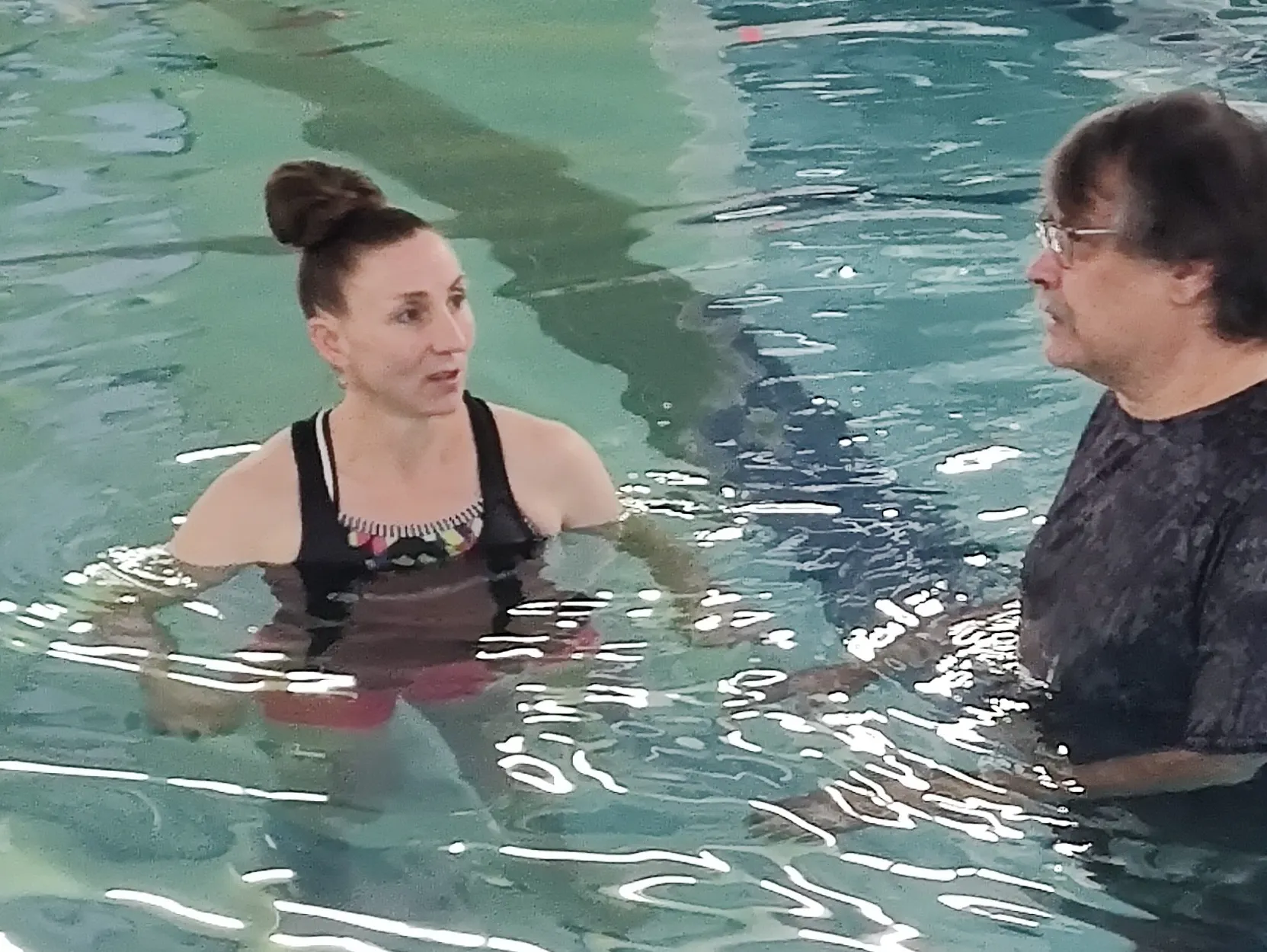 Two people are in a swimming pool, engaged in conversation while standing in the water.